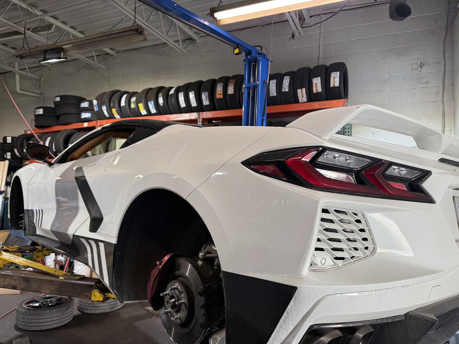 A white Corvette up on the lift in the Active Auto bay, racks of tires behind.